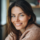 Femme souriante en pull brun clair, intérieur flou.
