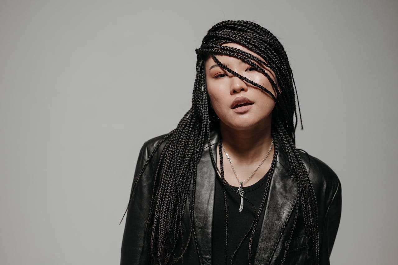 Close-up of a confident woman with braided hair and a leather jacket in studio setting.